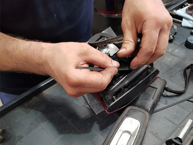 Another mechanic carefully removes seal on rear light unit Mechanic removes seal on light unit